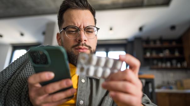 
		A sick man holding a cell phone and some pills
	